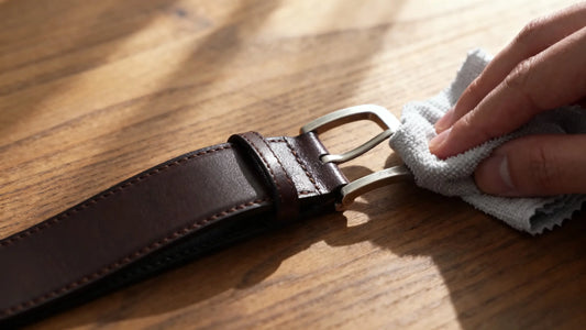 hand cleaning leather belt buckle with soft cloth on wooden table